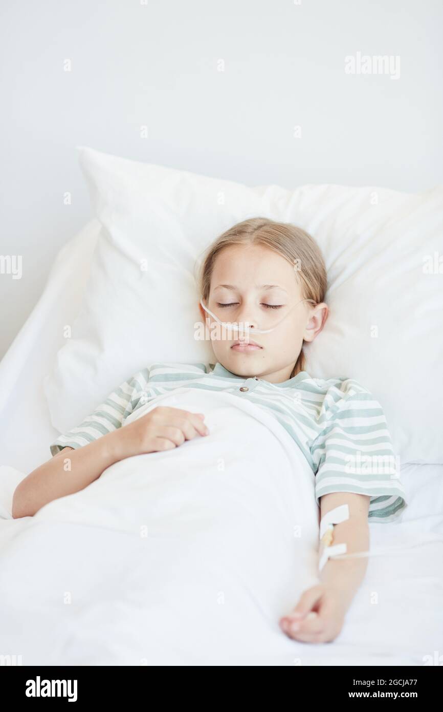 Vertical portrait of little girl laying in hospital bed with oxygen
