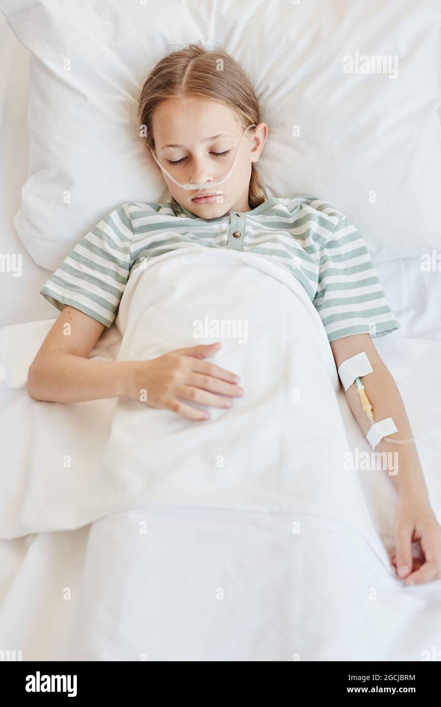 Vertical above view of child laying in hospital bed with oxygen support and IV drip while sleeping Stock Photo