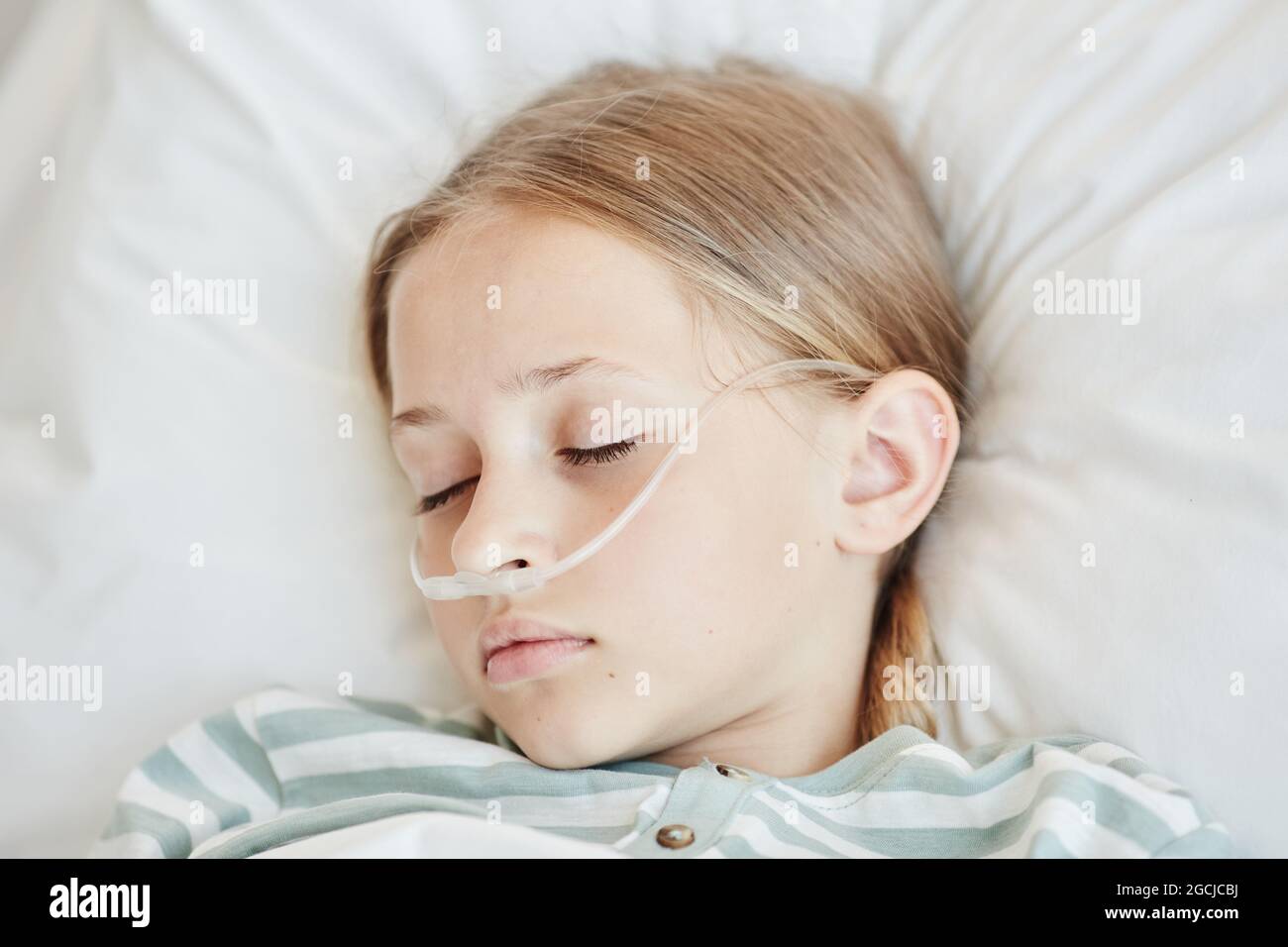 Minimal top down view at sleeping girl laying in hospital bed with oxygen support Stock Photo