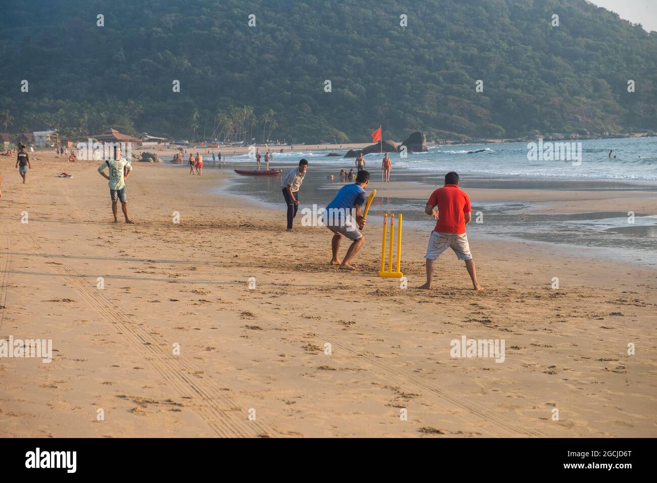 Group of Indian adults playing cricket on beach at sunset, Goa, India Stock Photo