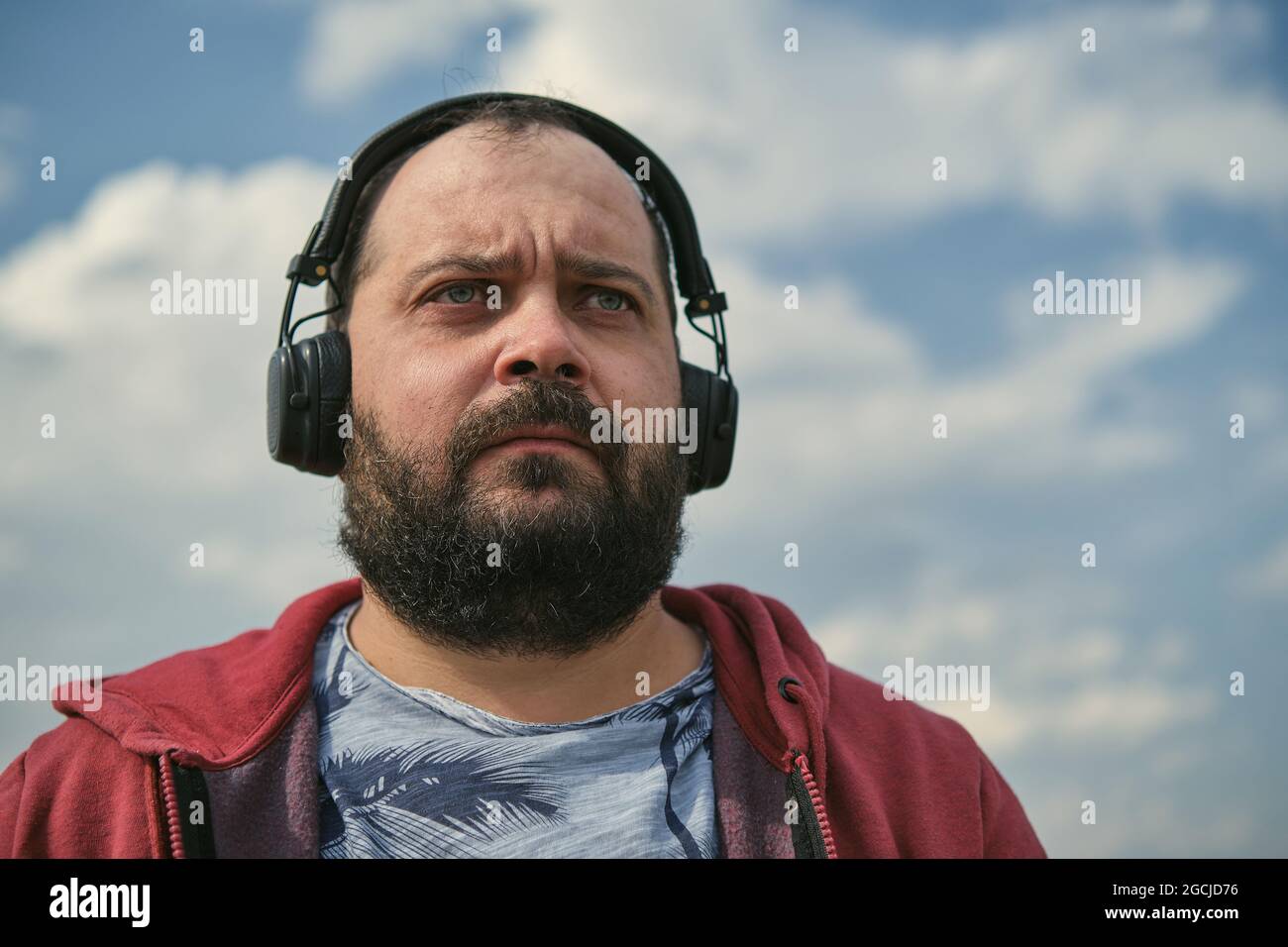 Middle-aged European man in headphones outdoors listening to music against the background of the sky Stock Photo