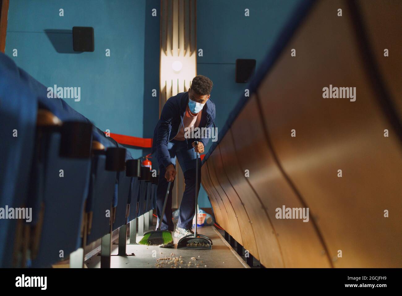 Young man cleaner sweeping floor in the cinema after the film, coronavirus concept. Stock Photo