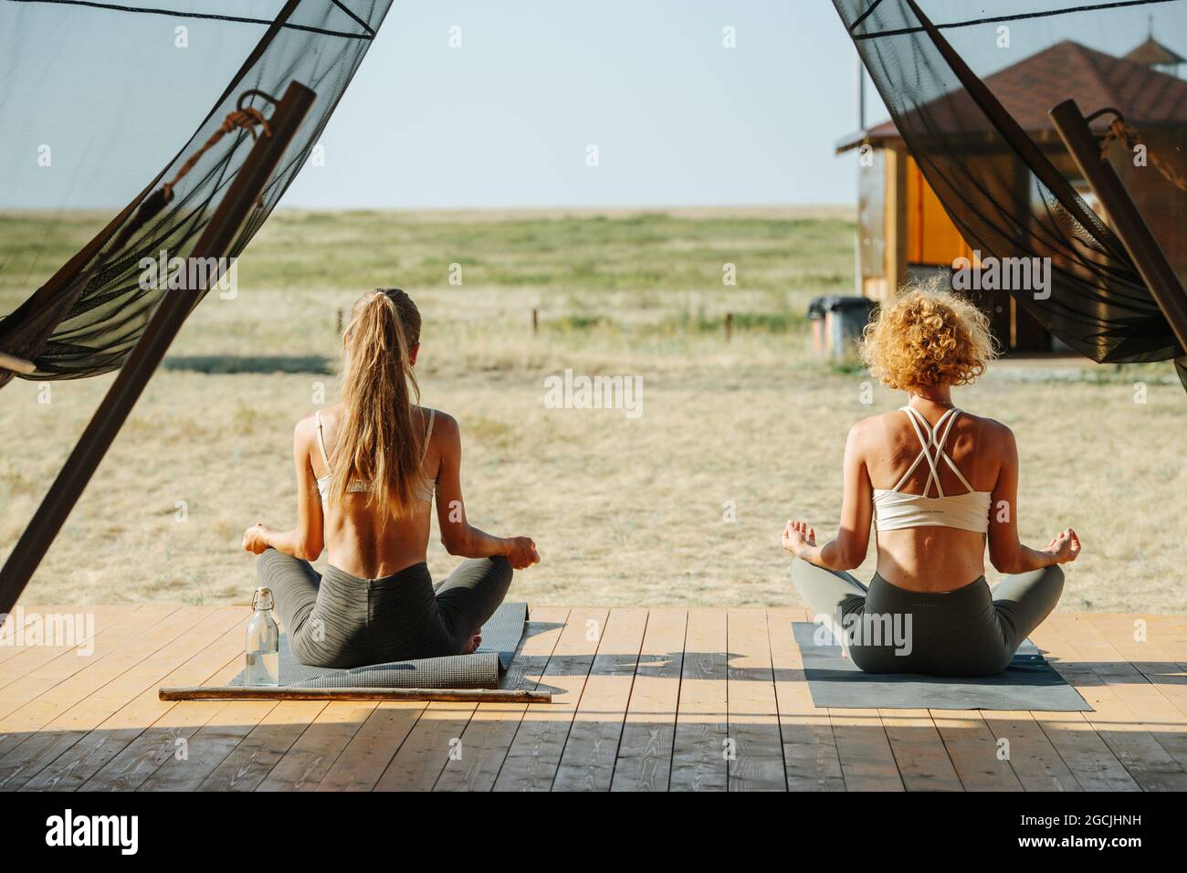 Two women meditating on a doorstep of a big tent, from behind