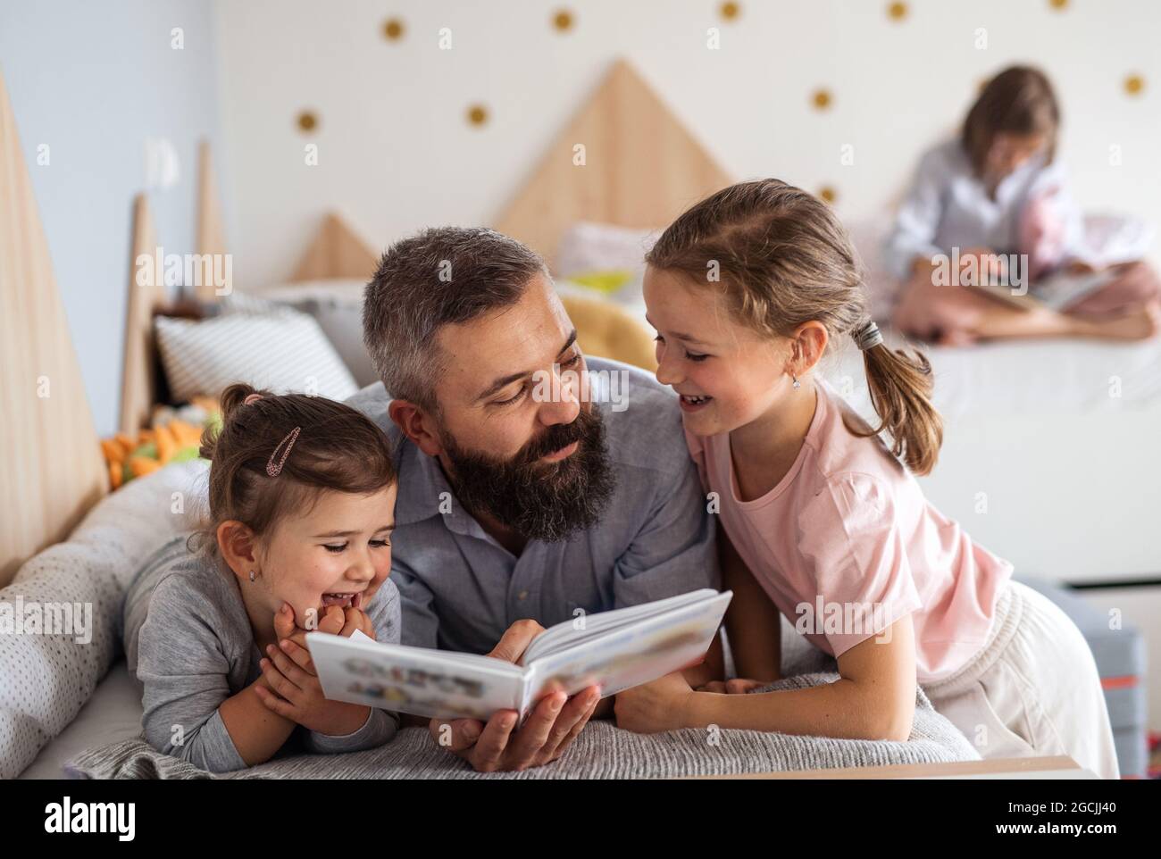 Father with three daughters indoors at home, reading a book. Stock Photo
