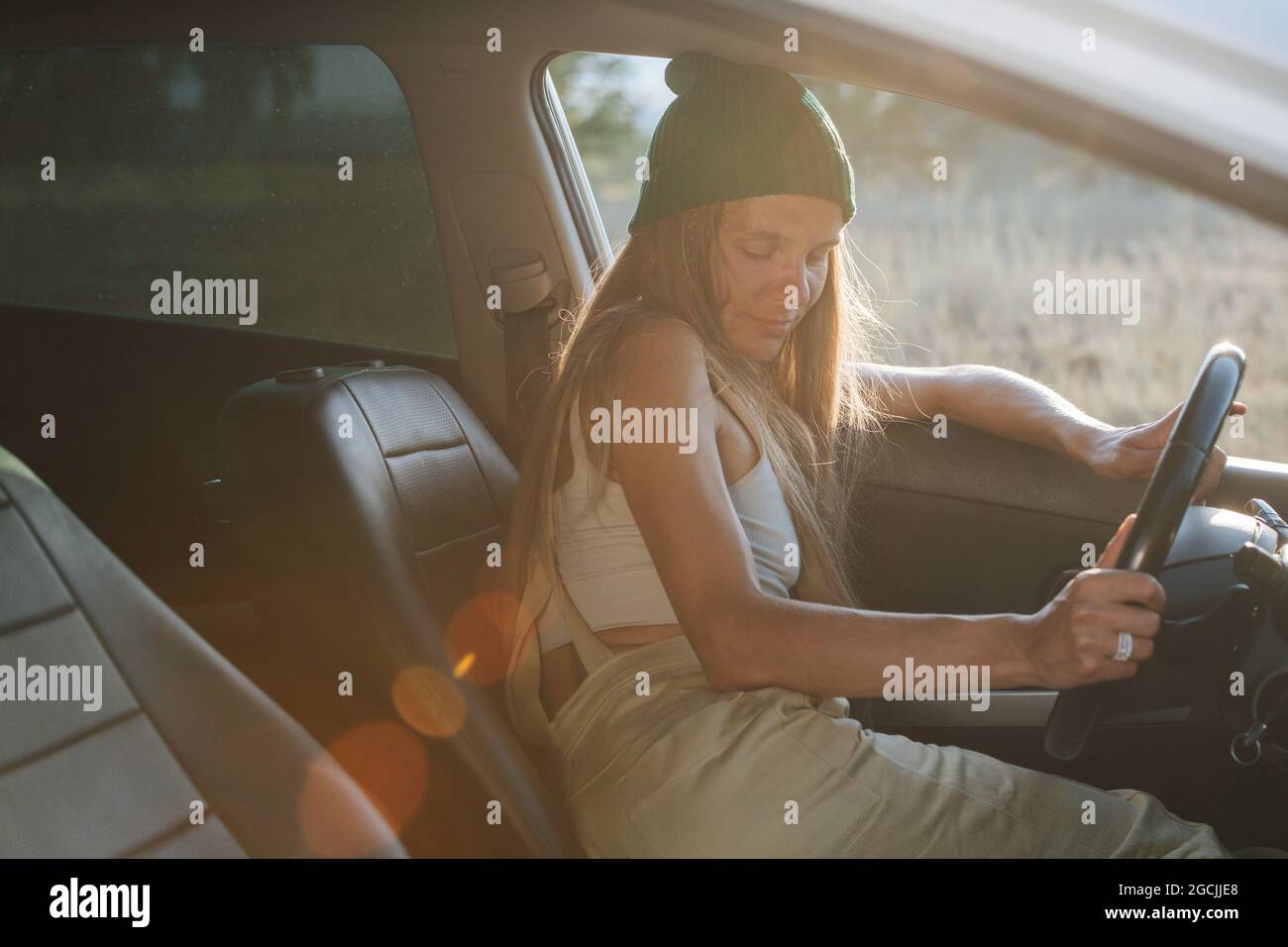 Tired woman in a watch cap napping in the car, leaning on window frame. Eyes closed. Stock Photo