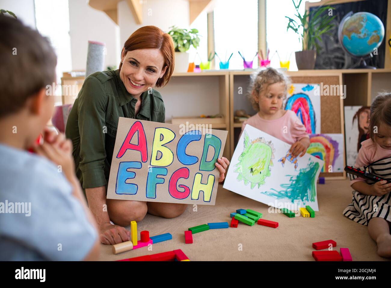 Group of small nursery school children with teacher on floor indoors in classroom, learning. Stock Photo