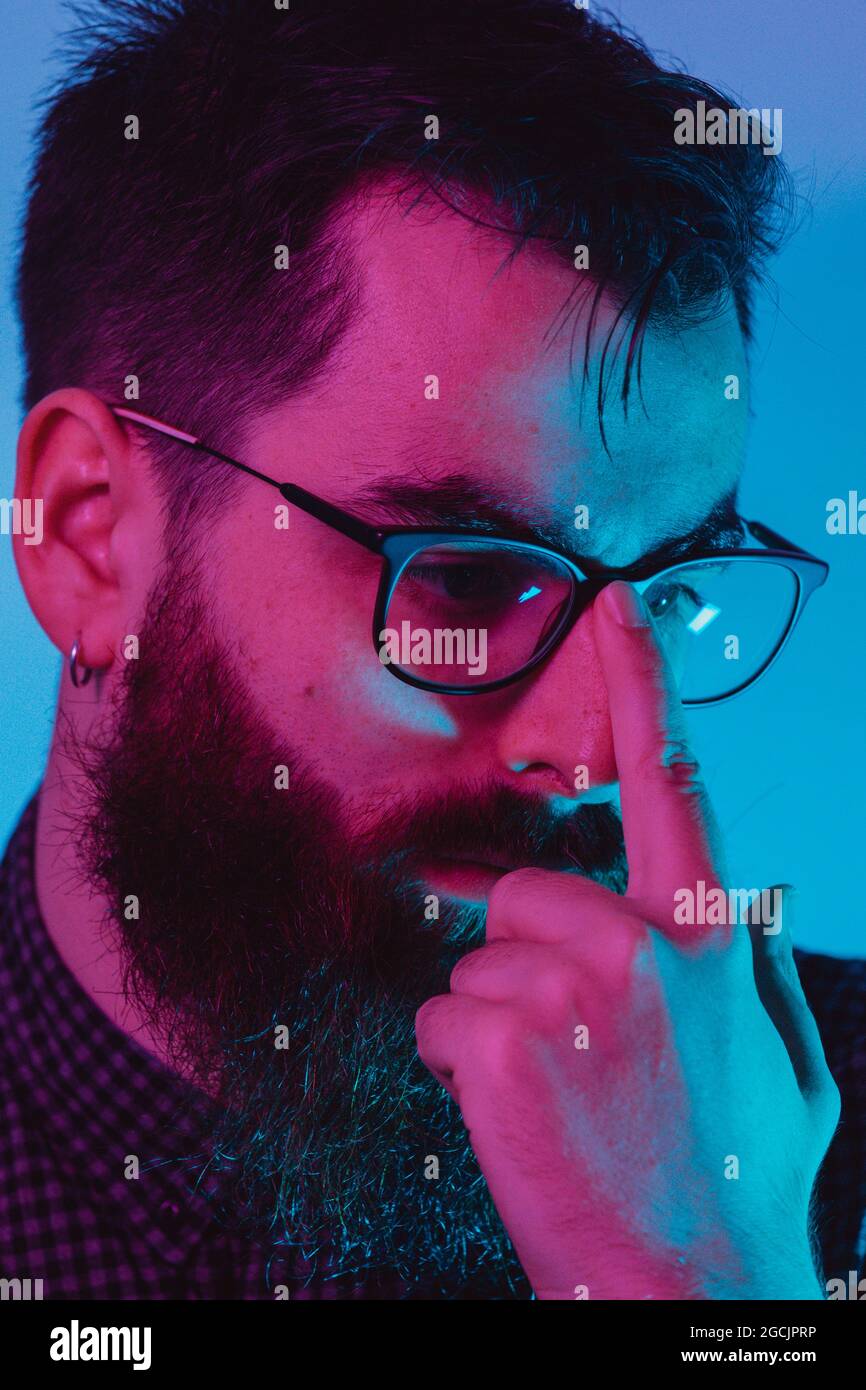 Vertical shot of a cool Caucasian guy with a beard and ear-piercing  adjusting his glasses Stock Photo - Alamy