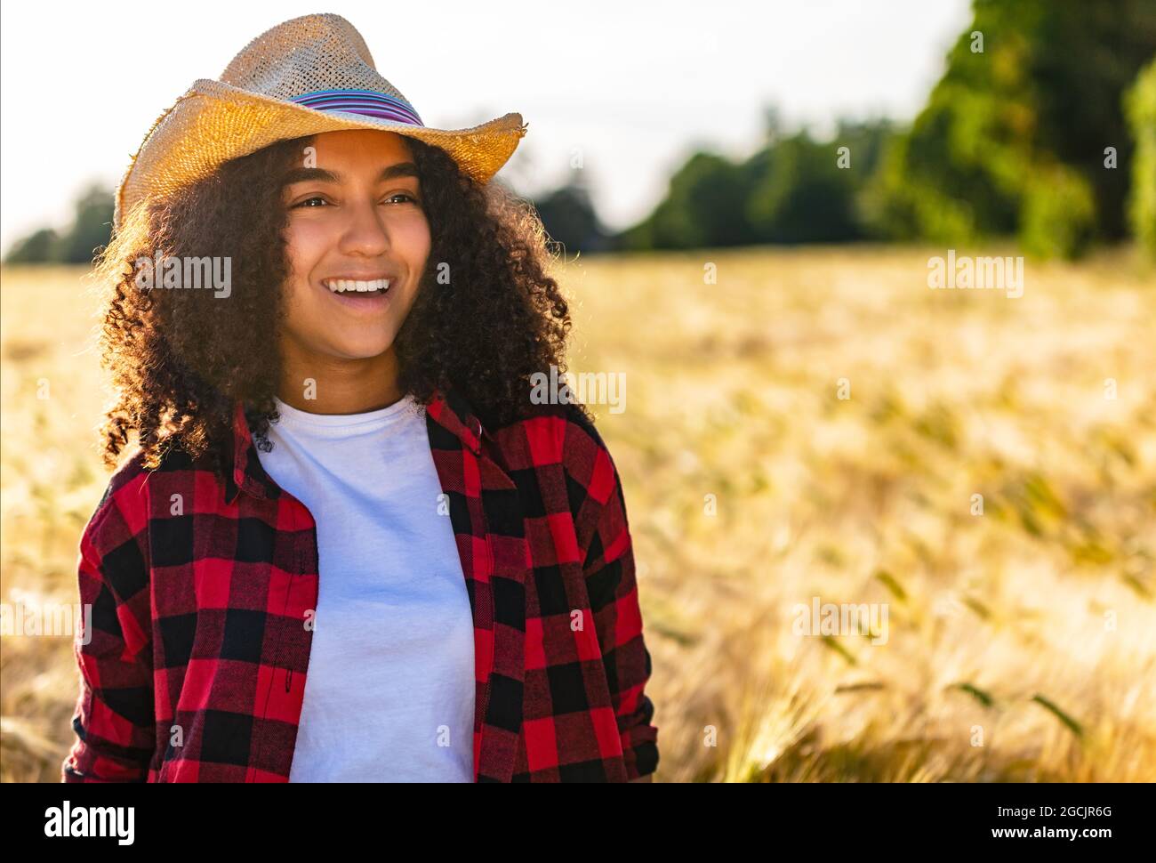 Beautiful happy mixed race African American biracial female girl teenager young woman with perfect teeth wearing cowboy hat and plaid shirt sitting in Stock Photo