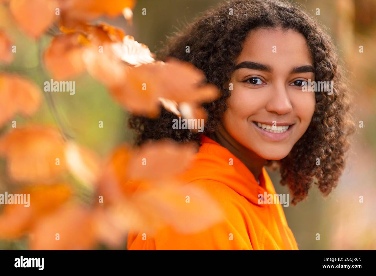 Outdoor portrait of beautiful happy mixed race biracial African American girl teenager female young woman smiling with perfect teeth wearing an orange Stock Photo