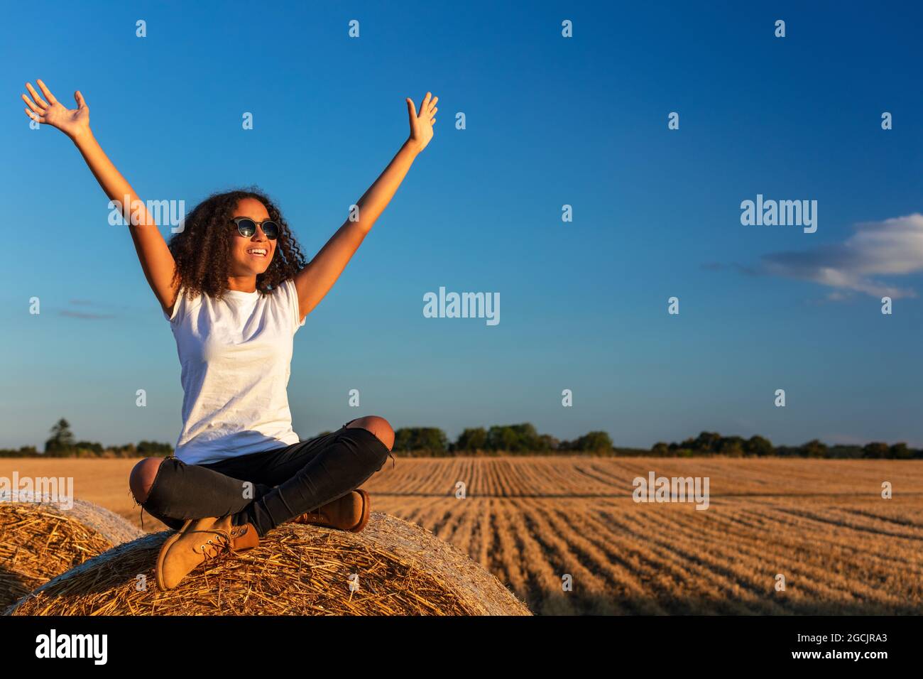 Beautiful, happy mixed race African American female girl child teenager young woman celebrating arms raised in sunshine wearing sunglasses and smiling Stock Photo