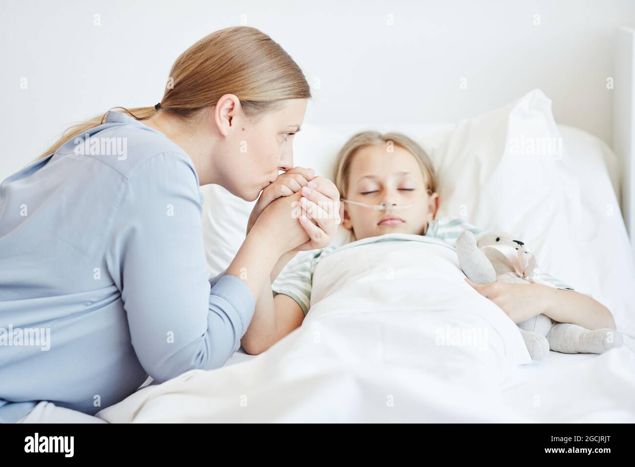 Side view portrait of caring mother holding hand of child in hospital room with oxygen support Stock Photo