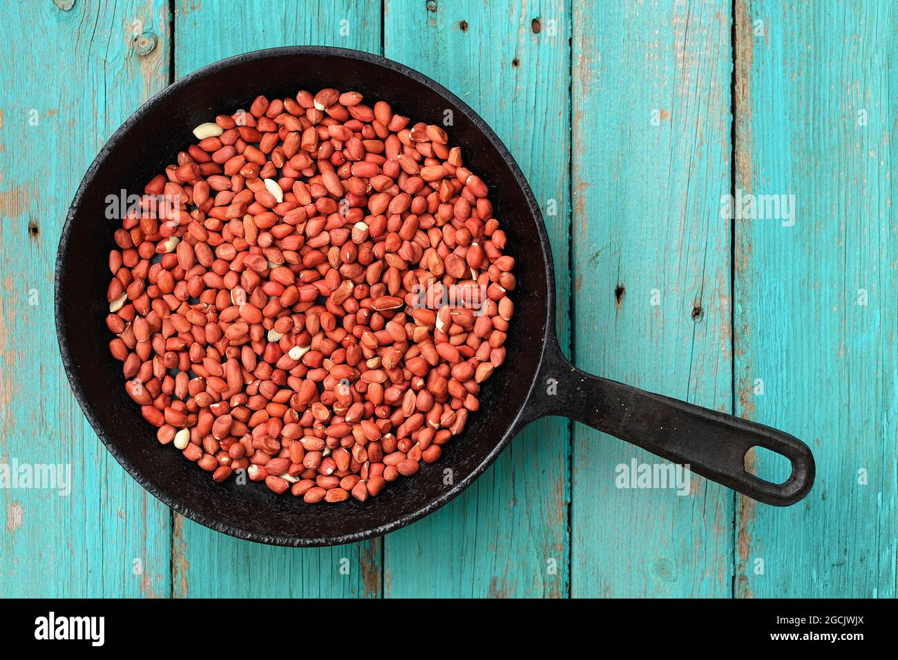 Whole fried pink peanuts in black cast iron pan on  turquoise table top view copyspace horizontal Stock Photo