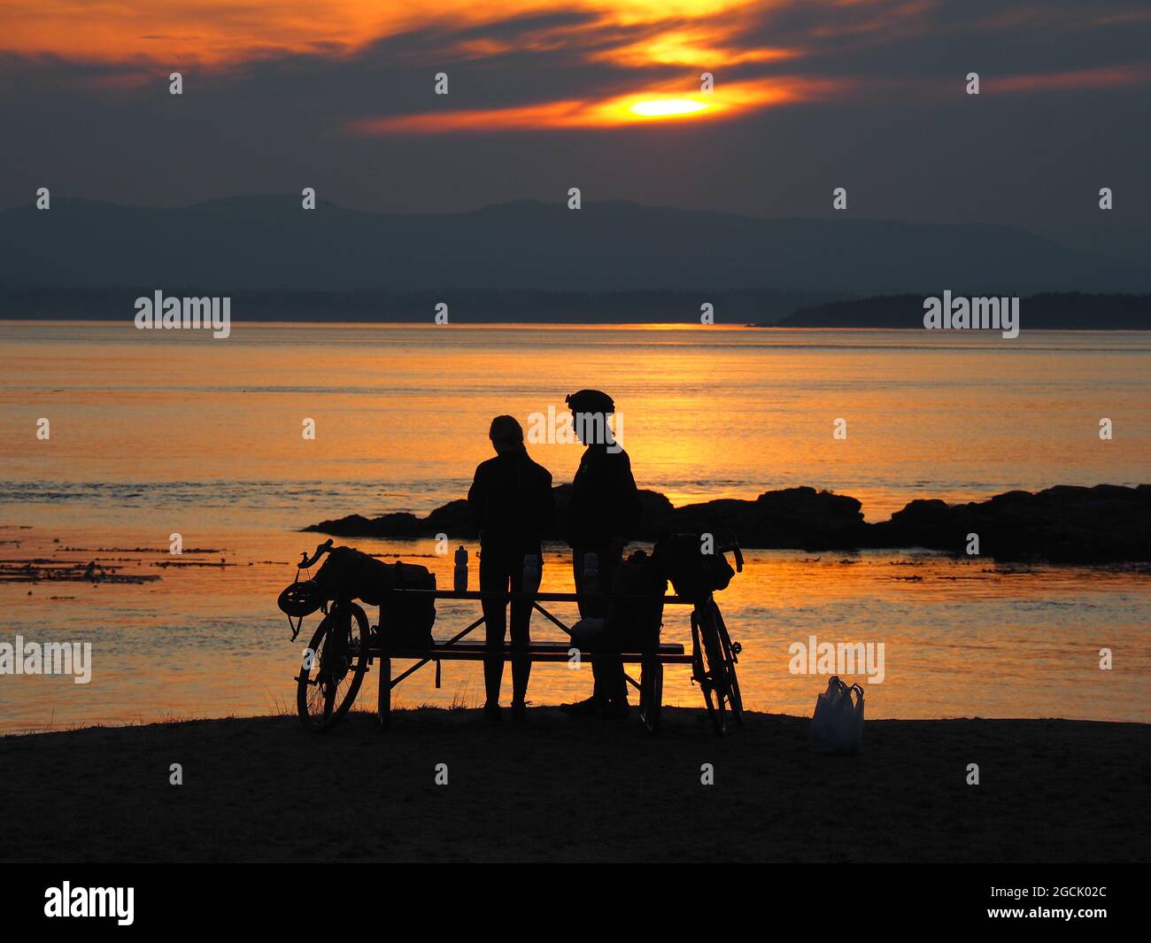 ORKA ISLAND, UNITED STATES - Aug 22, 2019: A couple with their bicycles enjoys the beautiful sunset at the beach while Stock Photo