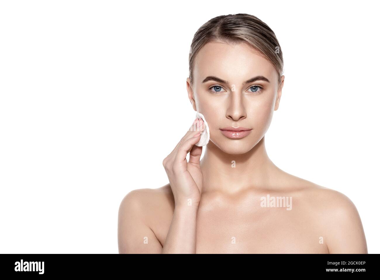 Beautiful woman using cotton pad to remove make up, looking at camera smiling. Studio shot on white background. Beauty and skincare concept. Stock Photo