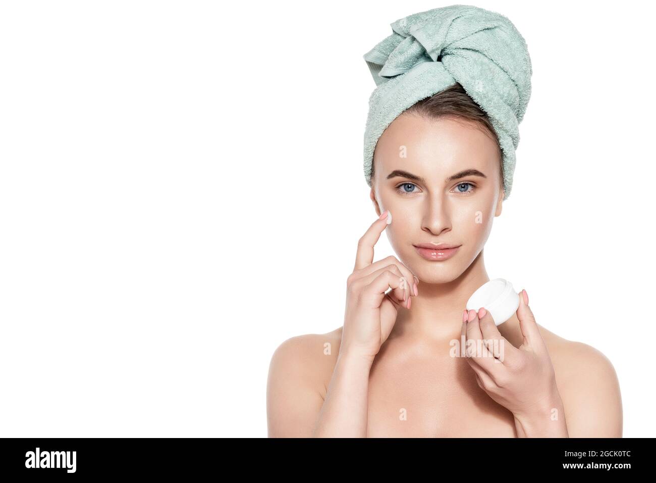 Beautiful young woman applying moisturiser face cream, looking at camera smiling. Studio shot on white background. Beauty and skincare concept. Stock Photo