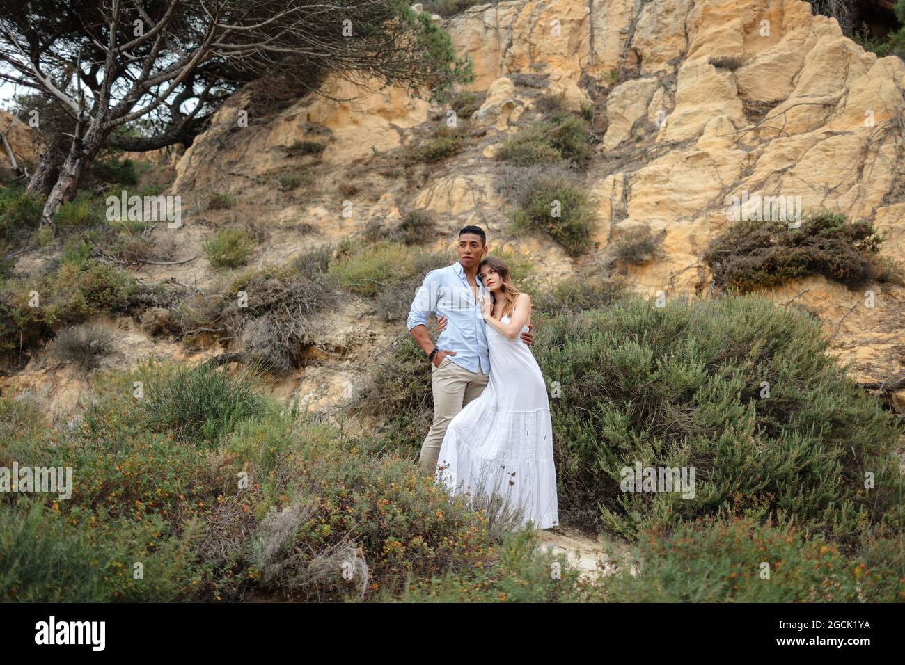 Diverse bride and groom embracing while standing in forest on wedding ...