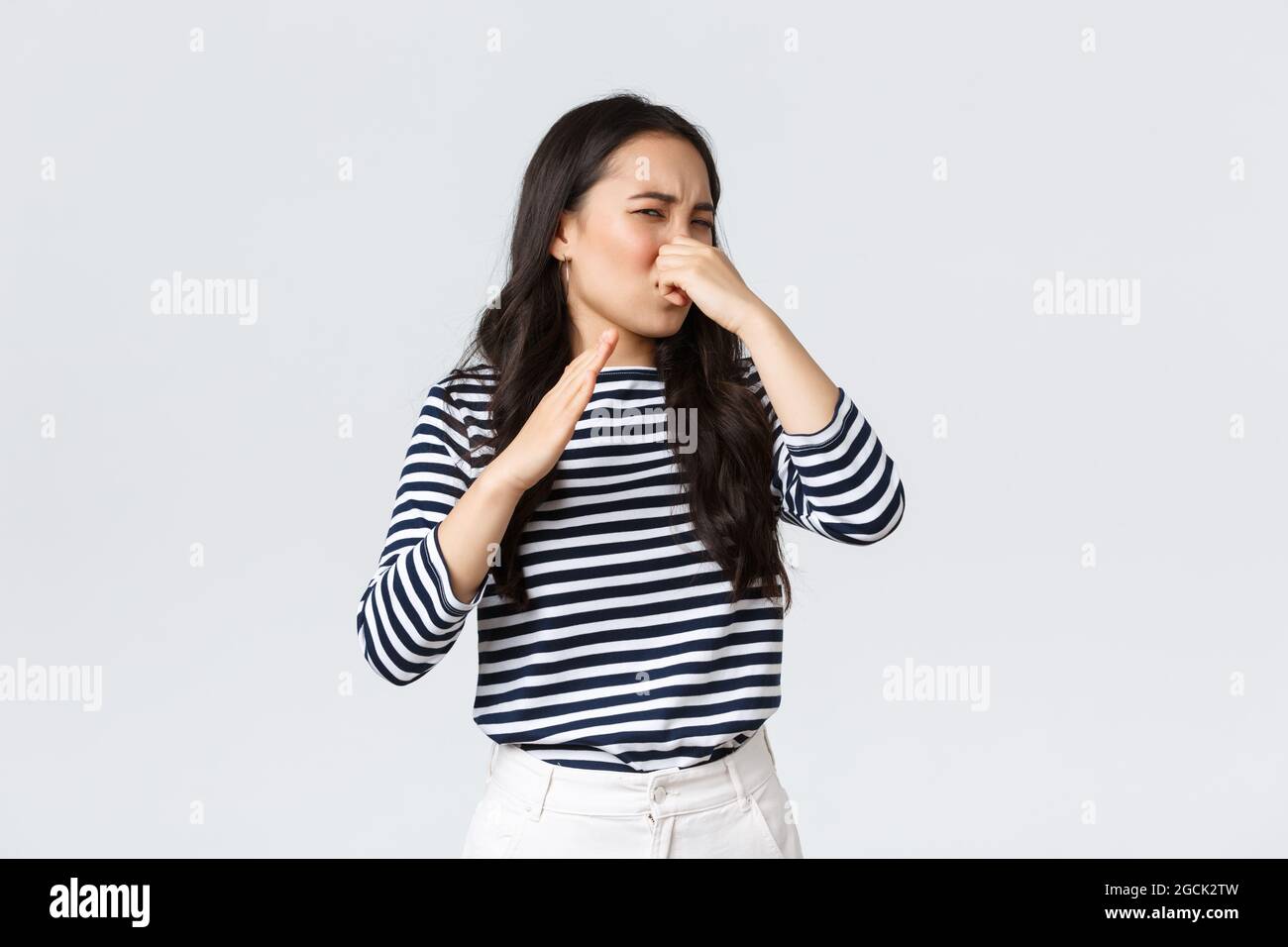 Lifestyle, beauty and fashion, people emotions concept. Disgusted korean girl shut nose and waving hand from disgust and aversion as sniff awful Stock Photo