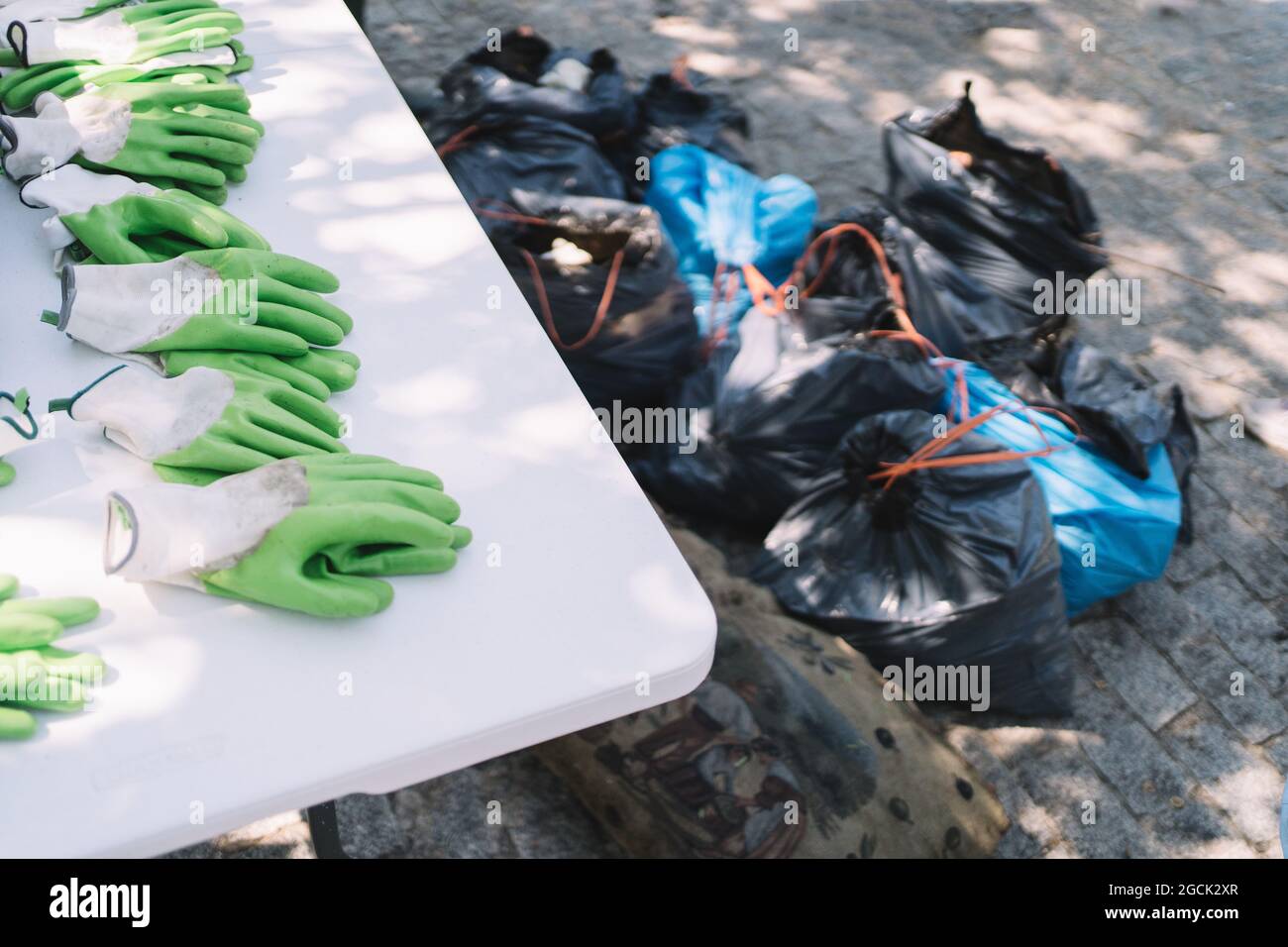 https://c8.alamy.com/comp/2GCK2XR/green-rubber-gloves-placed-on-table-near-heap-of-trash-bags-during-environmental-clean-up-campaign-in-summer-park-2GCK2XR.jpg