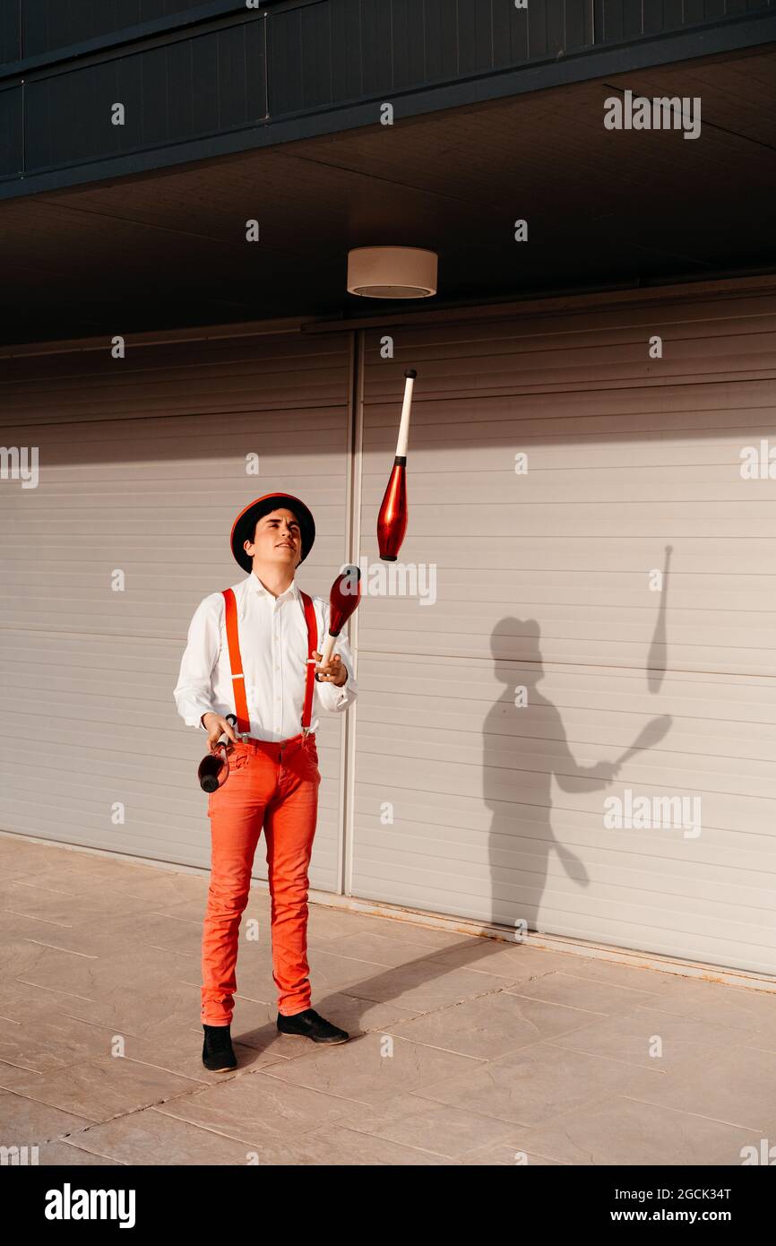 Skilled young male circus performer juggling with club on modern building Stock Photo