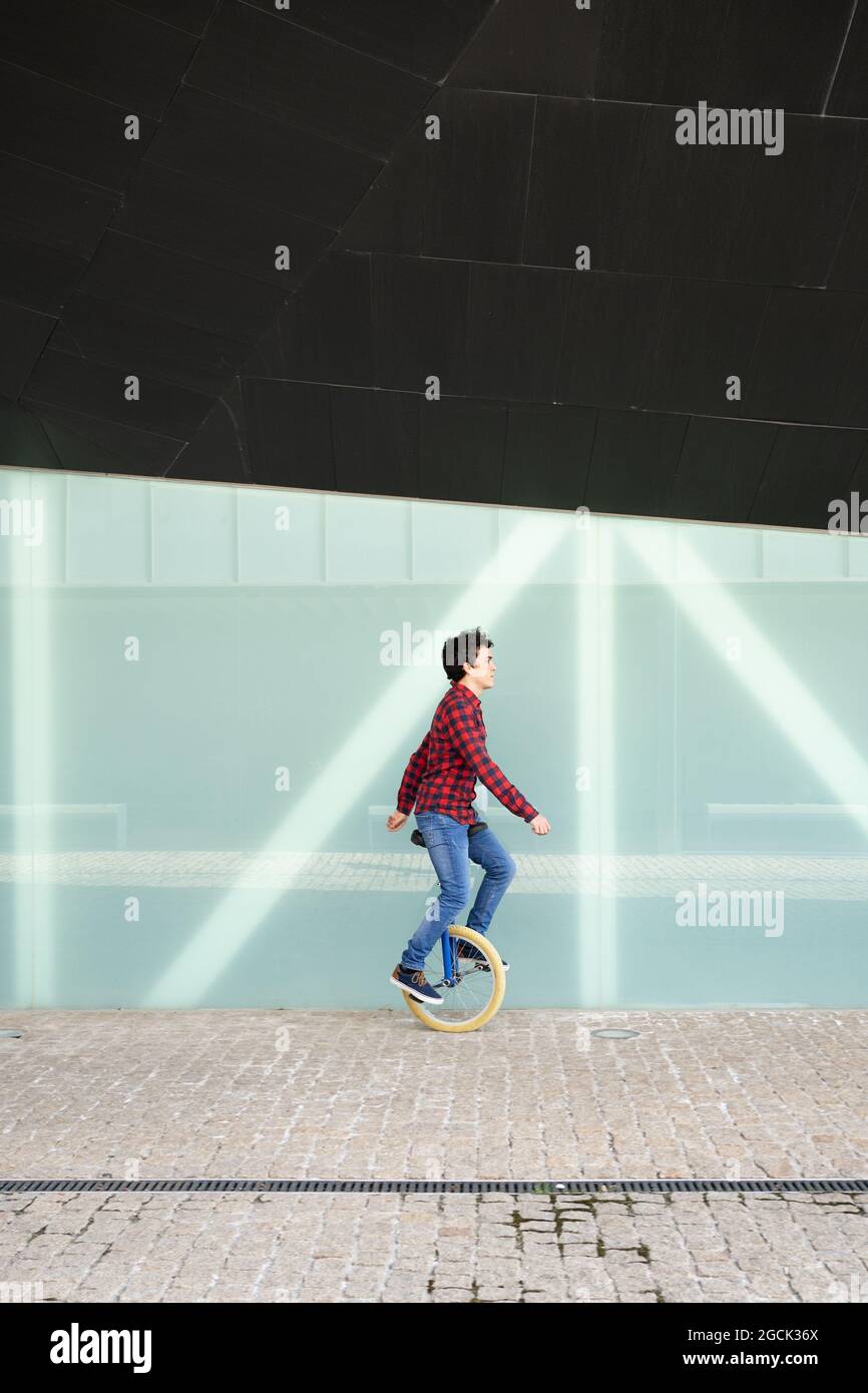 Full body side view of active young male in checkered shirt and jeans performing trick on