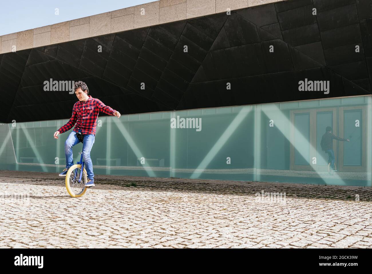 Full body side view of active young male in checkered shirt and jeans performing trick on