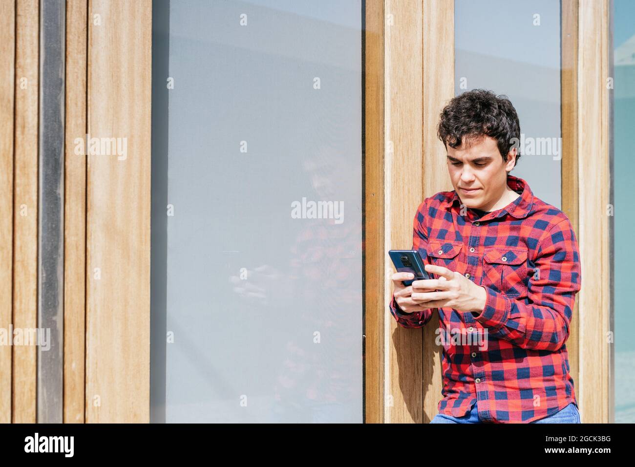 Young male in casual wear using smartphone while standing against modern urban building Stock Photo
