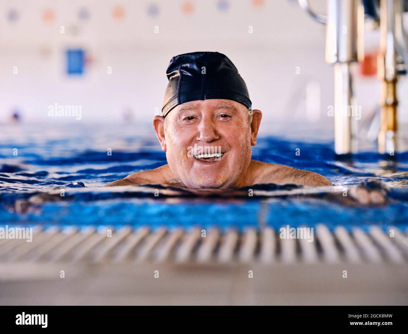 Delighted Middle Aged Male In Cap Swimming In Pool And Doing Exercises