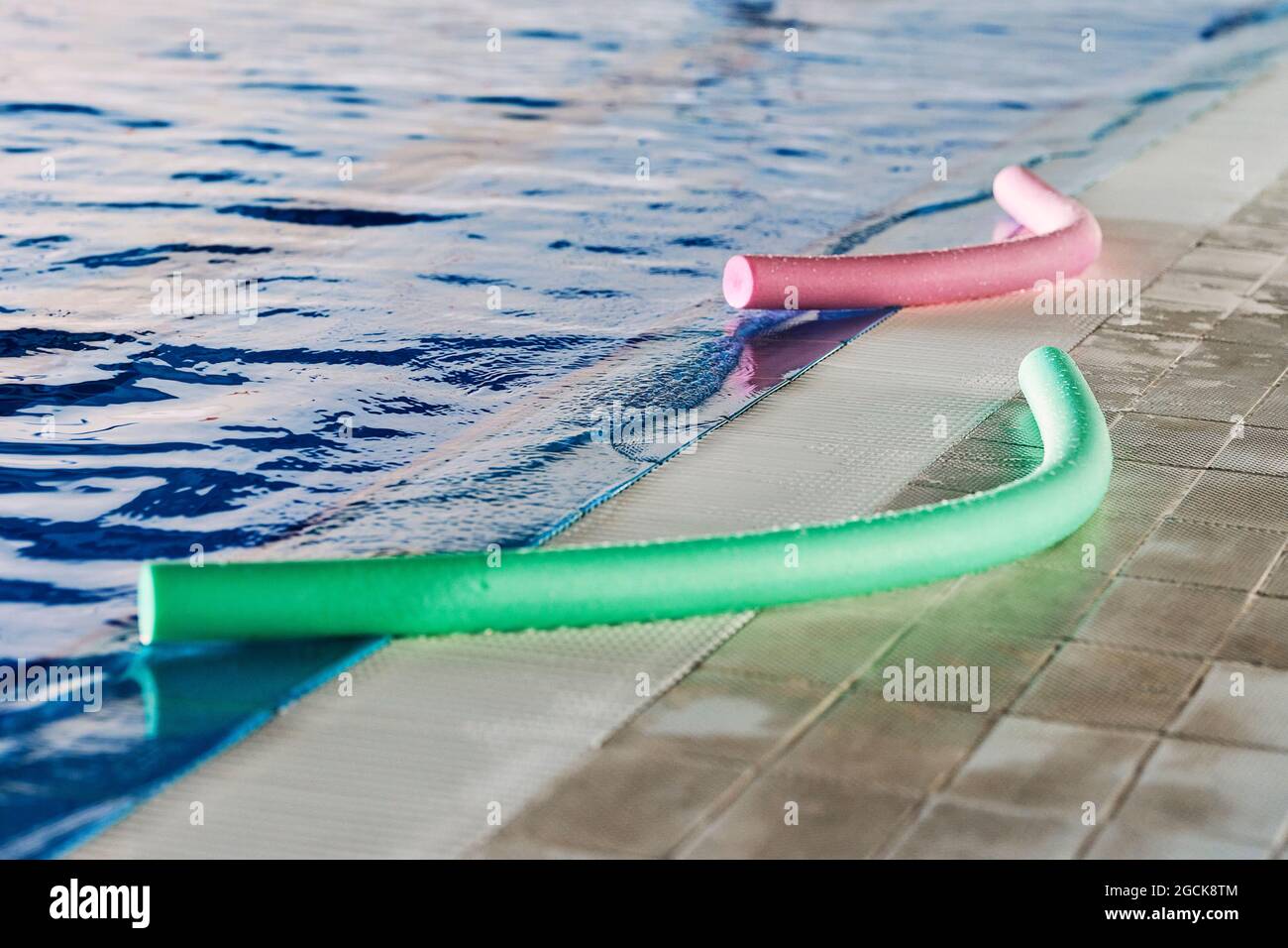 Green and pink foam aqua noodles placed near swimming pool for water