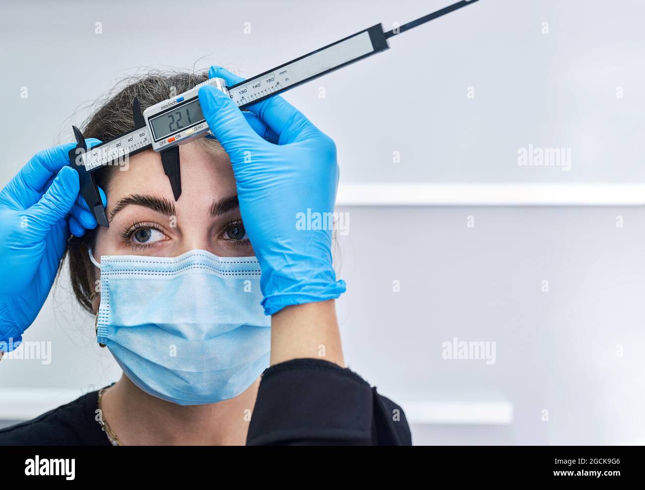 Cropped unrecognizable beautician in latex gloves using ruler to ...