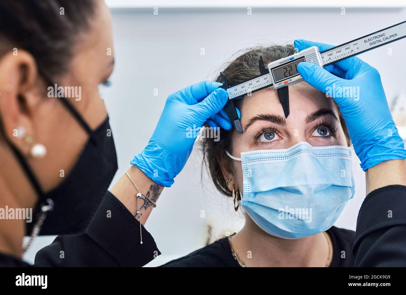 Cropped unrecognizable beautician in latex gloves using ruler to ...