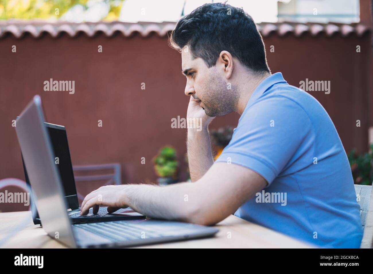 Profile of a young Caucasian man calling on a mobile phone while using a mobile phone holder to trade cryptocurrencies. Stock Photo
