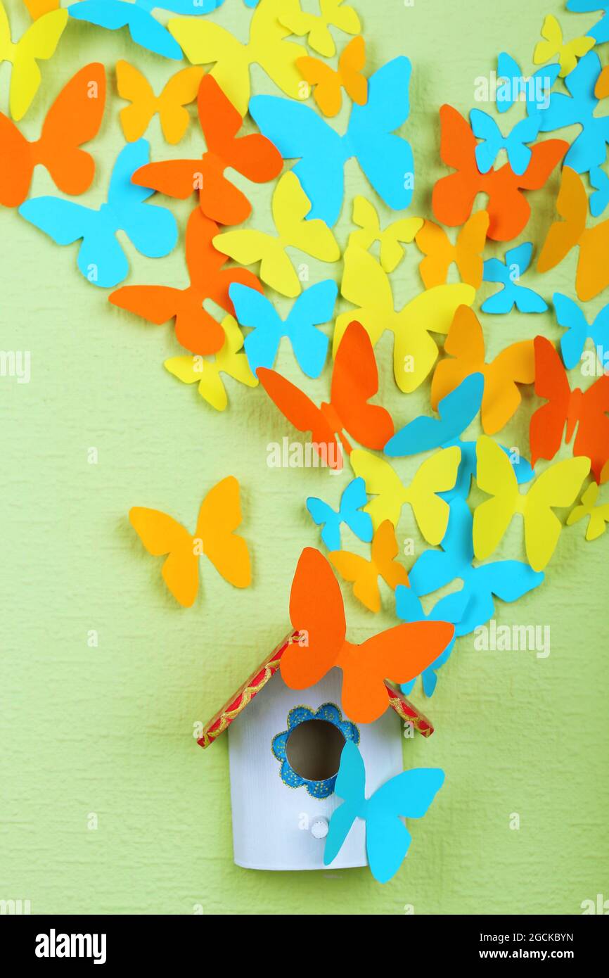 Paper butterflies fly out of nesting box on green wall background Stock
