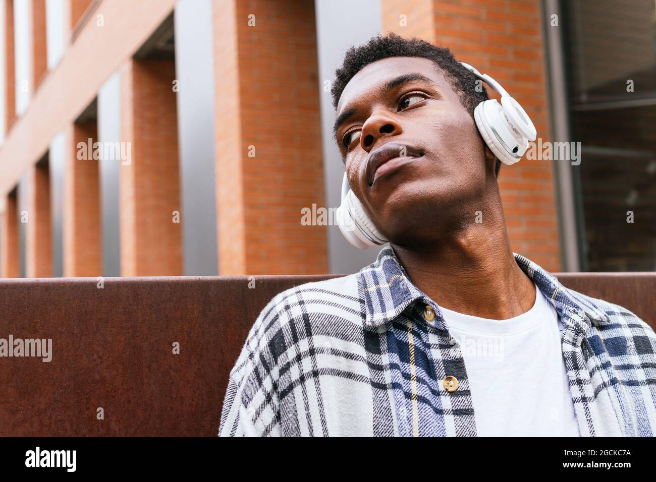 Unemotional African American stylish male standing with wireless headphones looking away in the city looking away Stock Photo