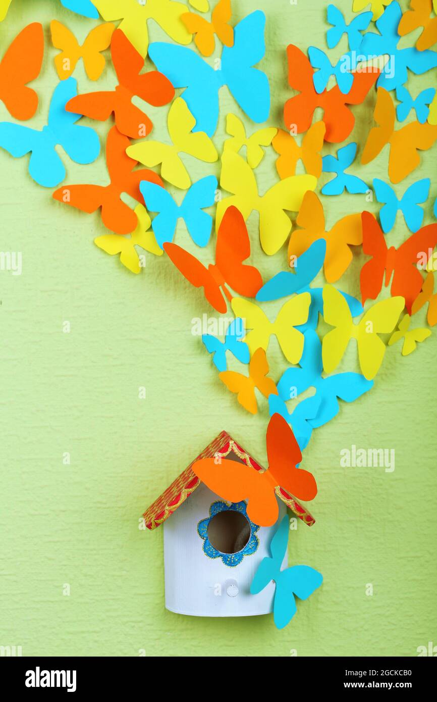 Paper butterflies fly out of nesting box on green wall background Stock