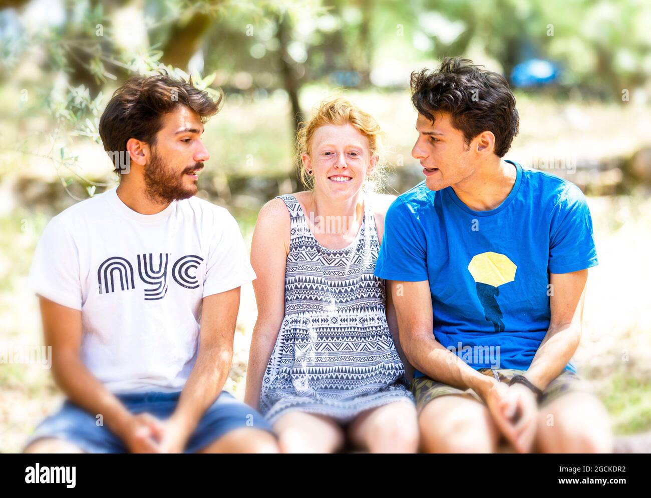 Two young white adults men and girl sit on wall Stock Photo