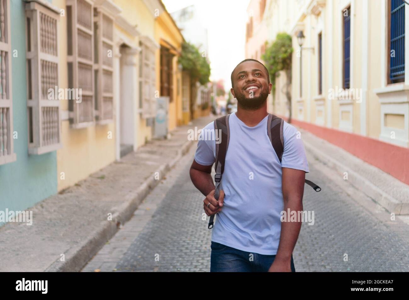 Smiling African man with backpack looking up while standing outdoors Stock Photo