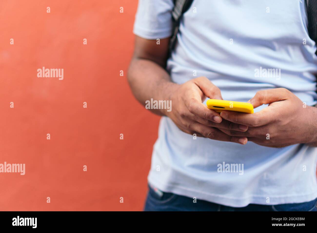 African man with smart phone next to a red wall Stock Photo