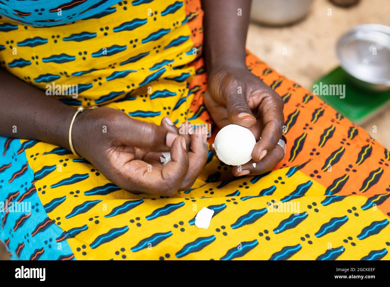 In this cloeup, a black woman or girl is peeling a boiled white egg,  letting the eggshells fall on the colouful fabric covering her lap Stock  Photo - Alamy