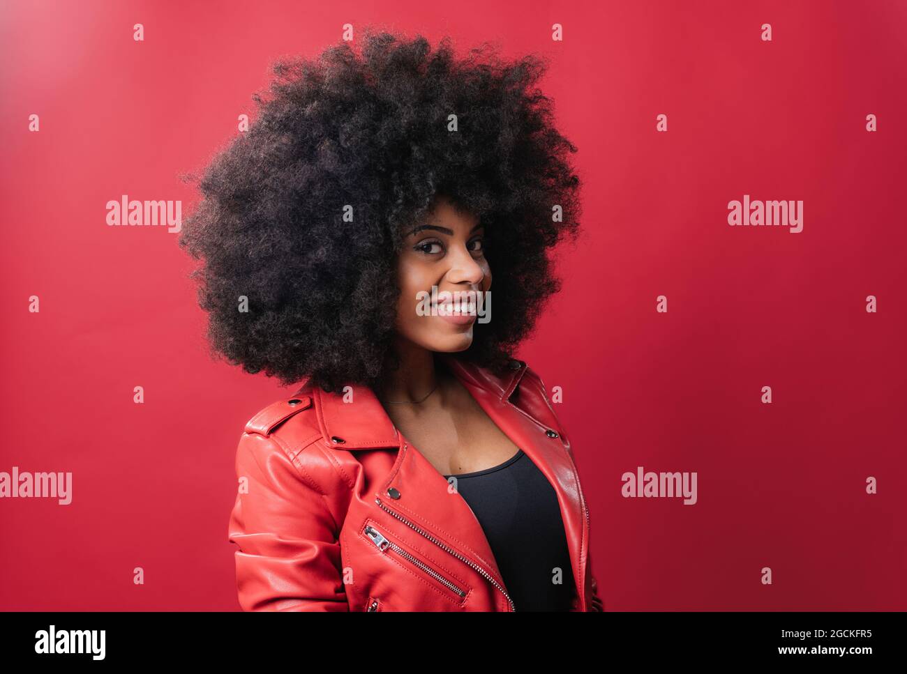 Delighted African American female with Afro hairstyle looking at camera on red background in studio Stock Photo
