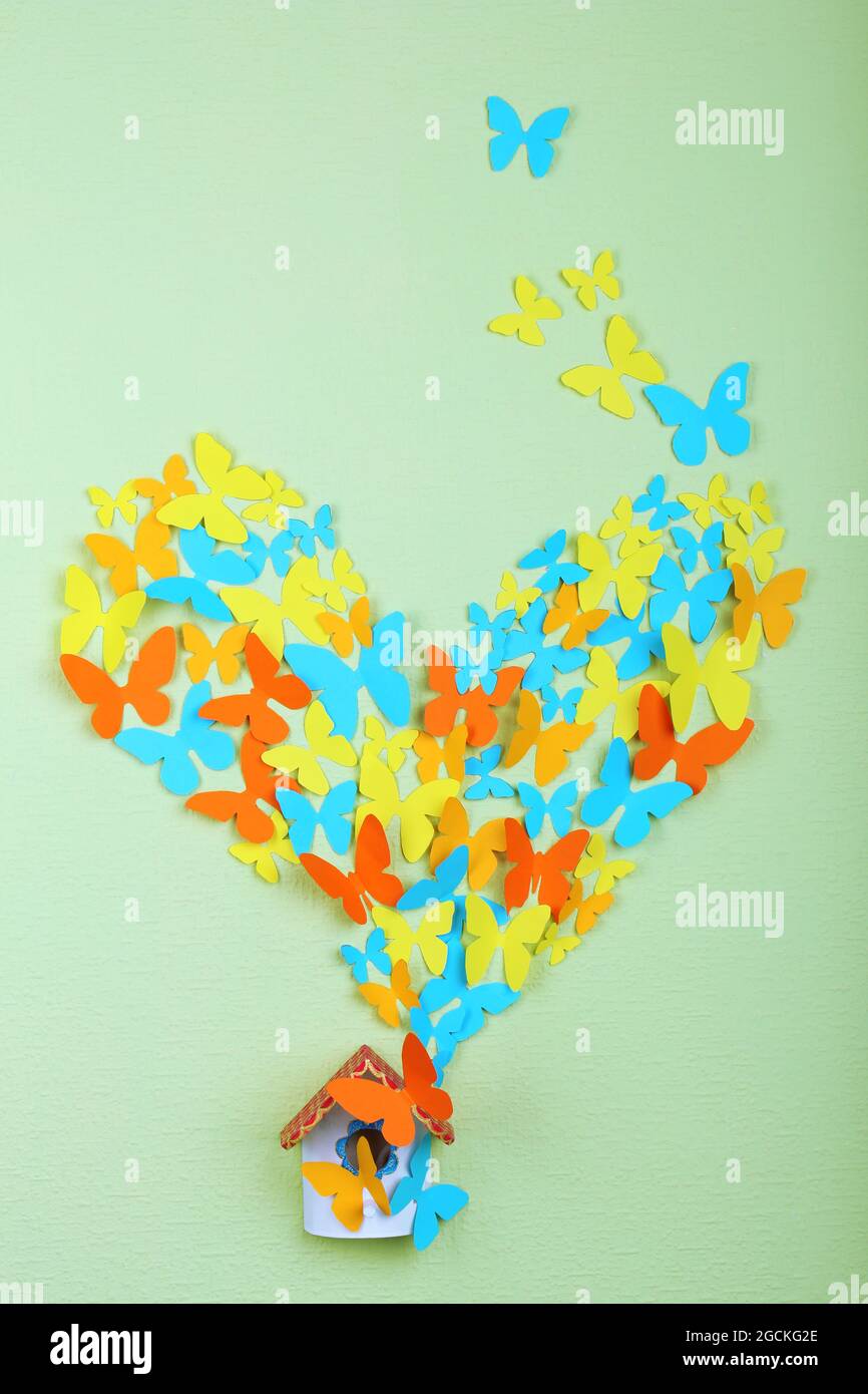 Paper butterflies fly out of nesting box on green wall background Stock