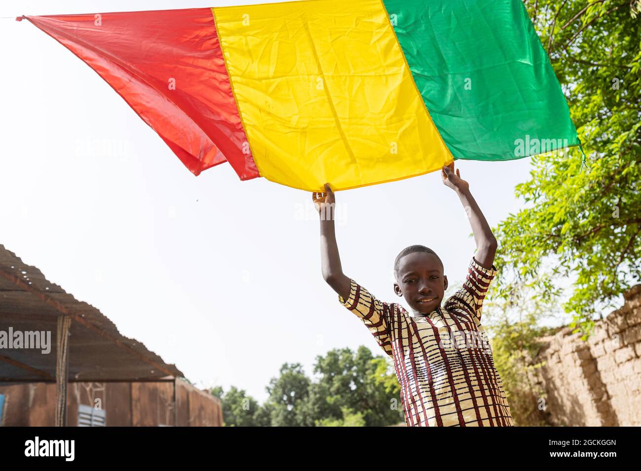 Smiling proud black boy, reaching out for his national flag hanging over the street during a traditional local African festivity Stock Photo