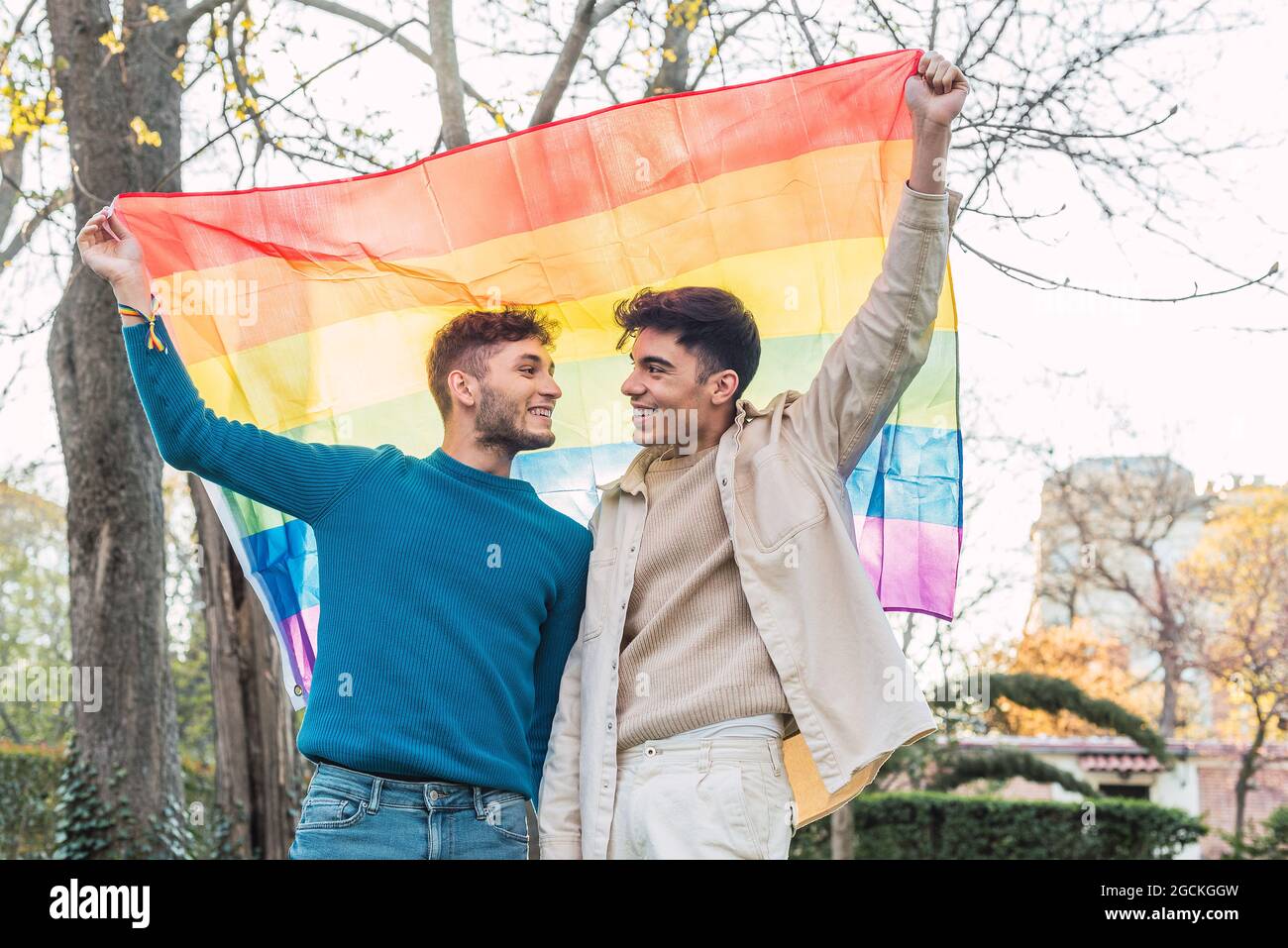 Low angle of cheerful couple of homosexual men standing with rainbow ...