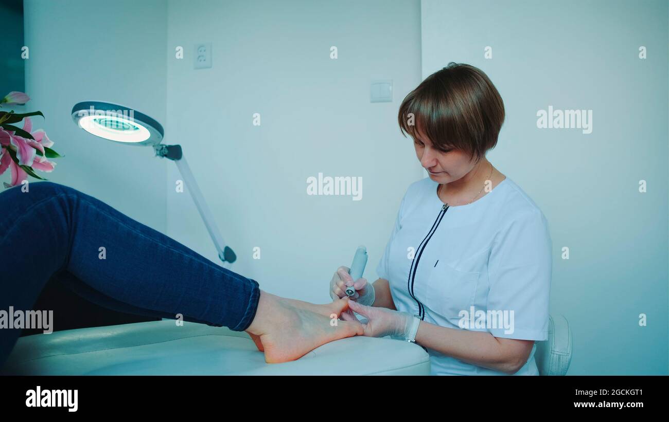 Cheerful manicurist making a hardware pedicure for woman. She grinding nails of the woman in beauty spa salon. Stock Photo