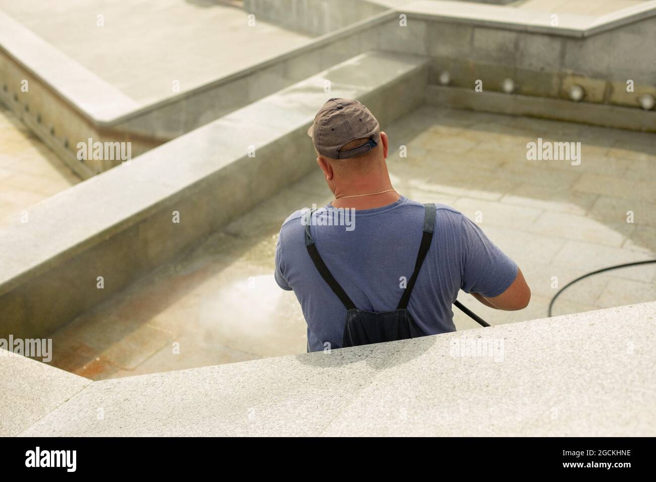 The worker washes the surface from rust. The man washes away the dirt with the help of the pressure of water. City services are cleaning the fountain. Stock Photo