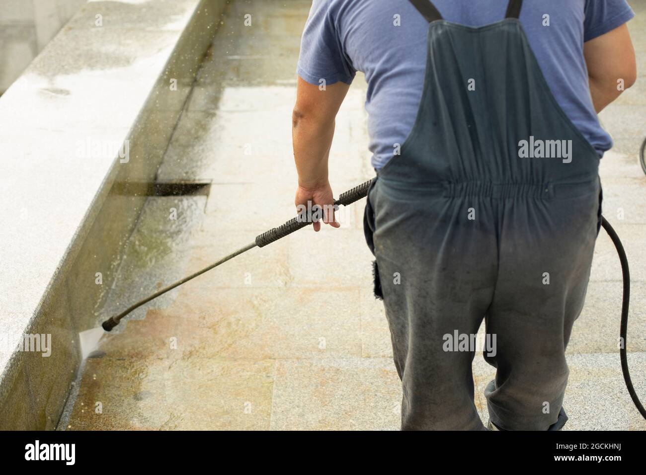 The worker washes the surface from rust. The man washes away the dirt with the help of the pressure of water. City services are cleaning the fountain. Stock Photo
