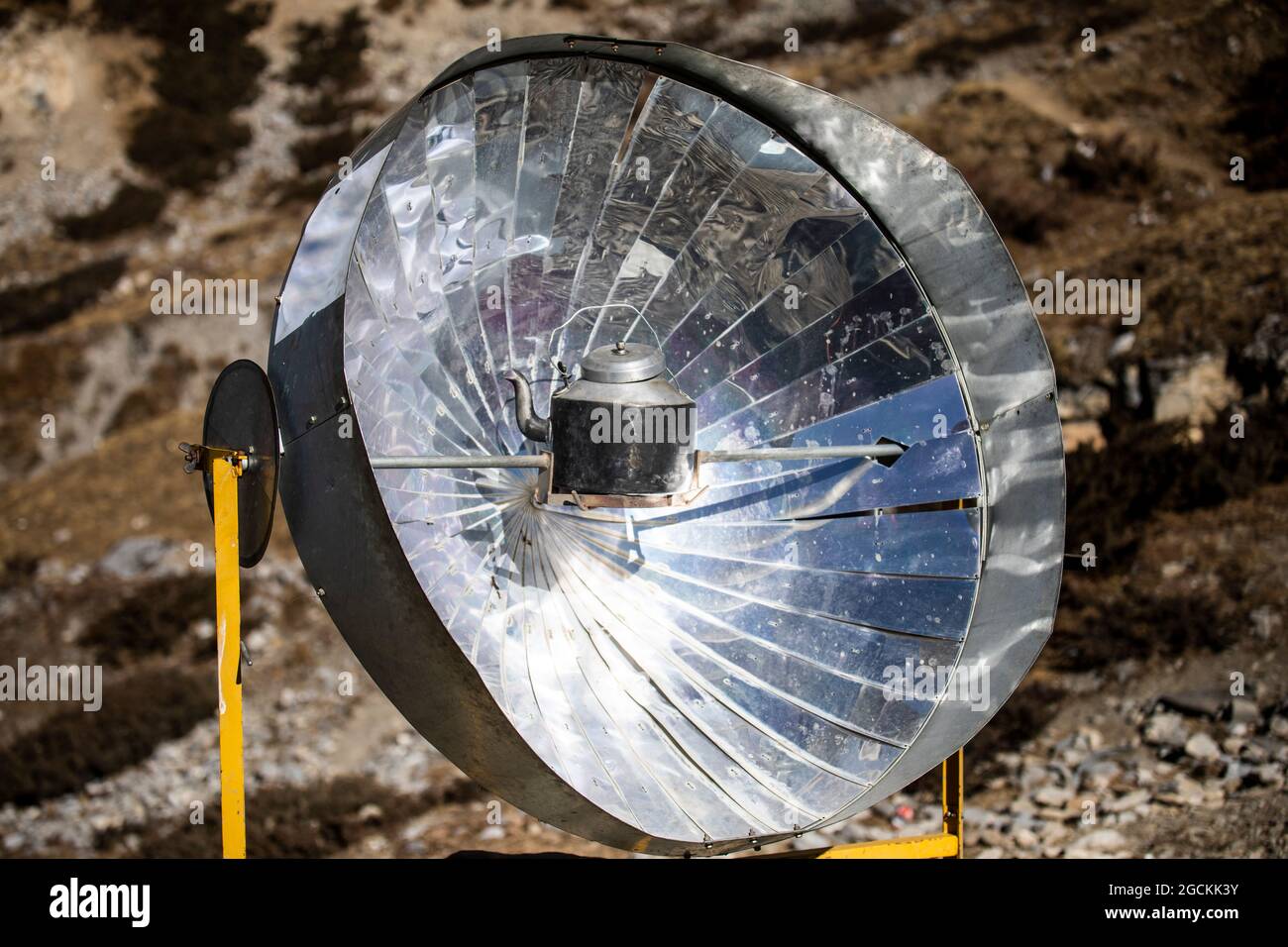 Water boiling in metal kettle placed on solar cooker on rocky ground in