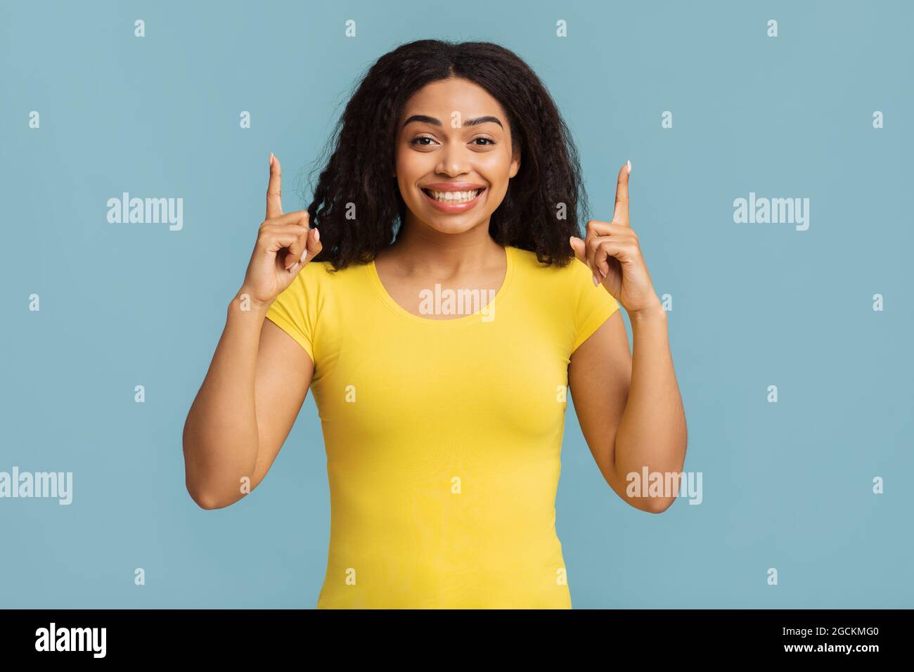 Look up. Excited african american lady pointing fingers upward showing something posing standing over blue background Stock Photo