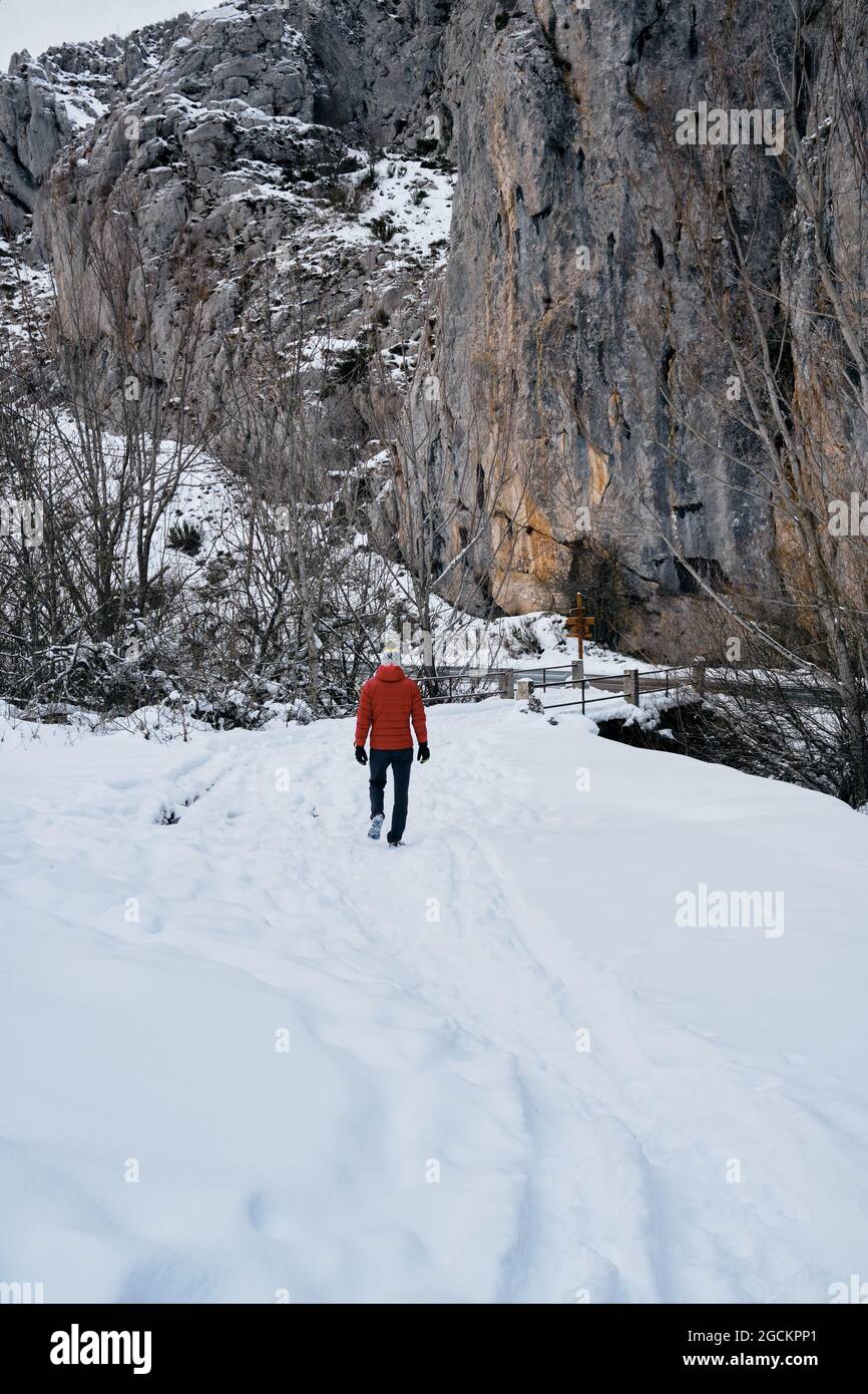 View from behind a man with red coat walking through the snowy mountains Stock Photo