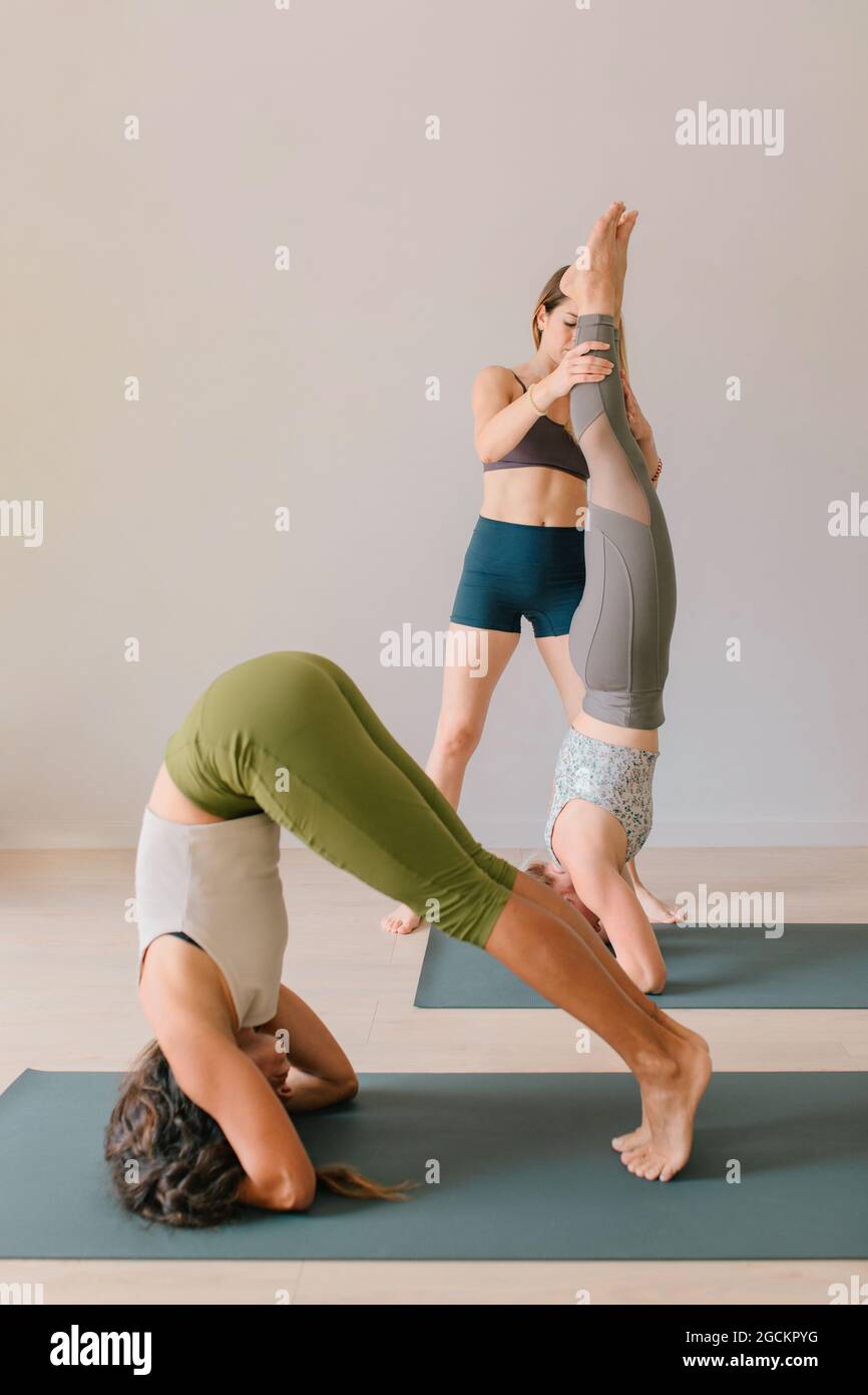Female yoga coach helping Woman balancing in Supported Headstand pose during yoga class in studio Stock Photo