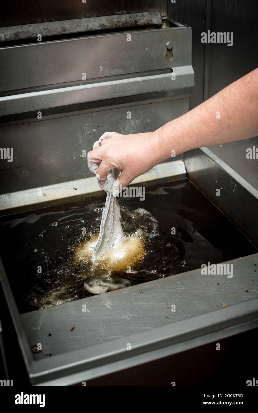 Crop unrecognizable cook preparing fish in oil in deep fryer while